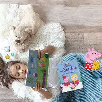 Ein junges Mädchen liegt mit einem Teddybär auf einem flauschigen Teppich und liest ein Peppa Pig-Buch. Ein personalisiertes Buch mit dem Titel "Sophie" und Peppa Pig-Illustrationen liegen neben ihr.