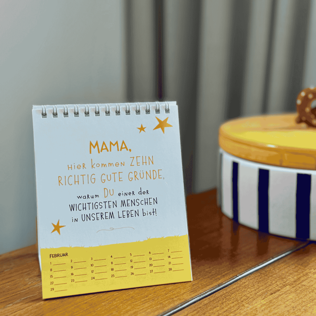 Ein kleiner spiralgebundener Kalender steht auf einer hölzernen Unterlage. Auf der sichtbaren Seite steht in deutscher Sprache geschrieben: Mama, hier kommen zehn richtig gute Gründe, warum du einer der wichtigsten Menschen in unserem Leben bist! Dies ist eine gute Geschenkidee.