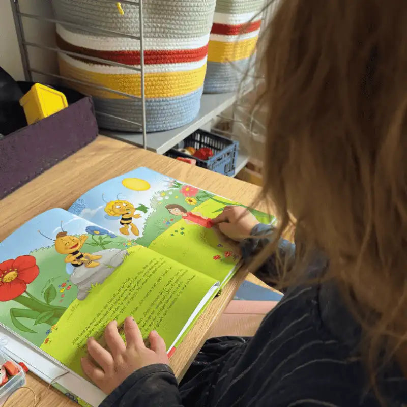 Mädchen blättert in illustriertem Bilderbuch mit Biene Maja.
