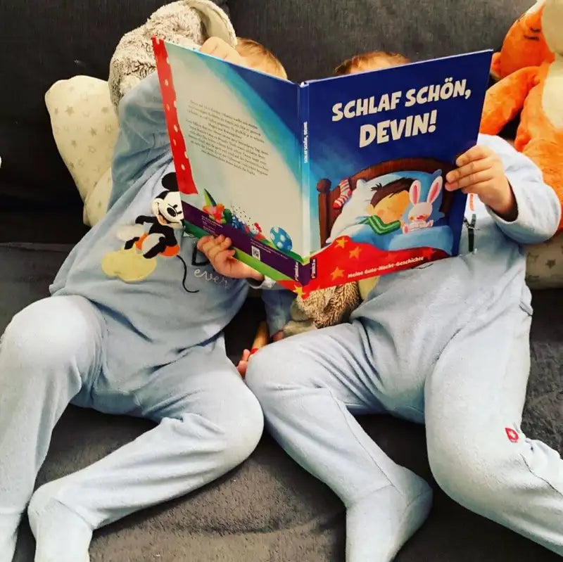 Zwei Kleinkinder schauen sich das Buch Schlaf Schön, Devin im Bett liegend an