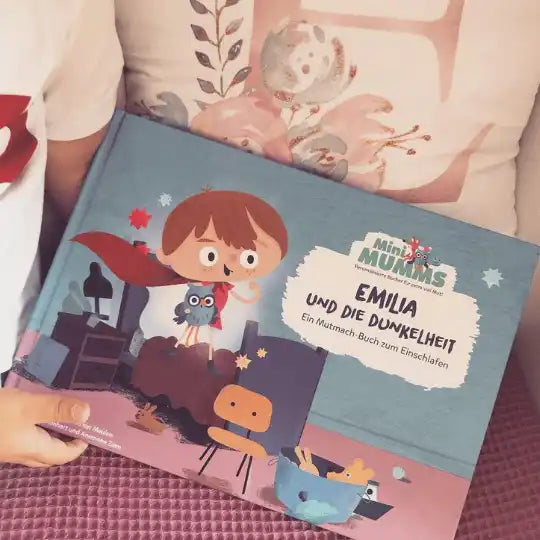 Ein Kind hält das Kinderbuch Dein Mutmach-Buch zum Einschlafen in der Hand, in dem Eule Molly Minimumm und ein Mädchen mit einem roten Umhang auf einem nächtlichen Cover zu sehen sind.