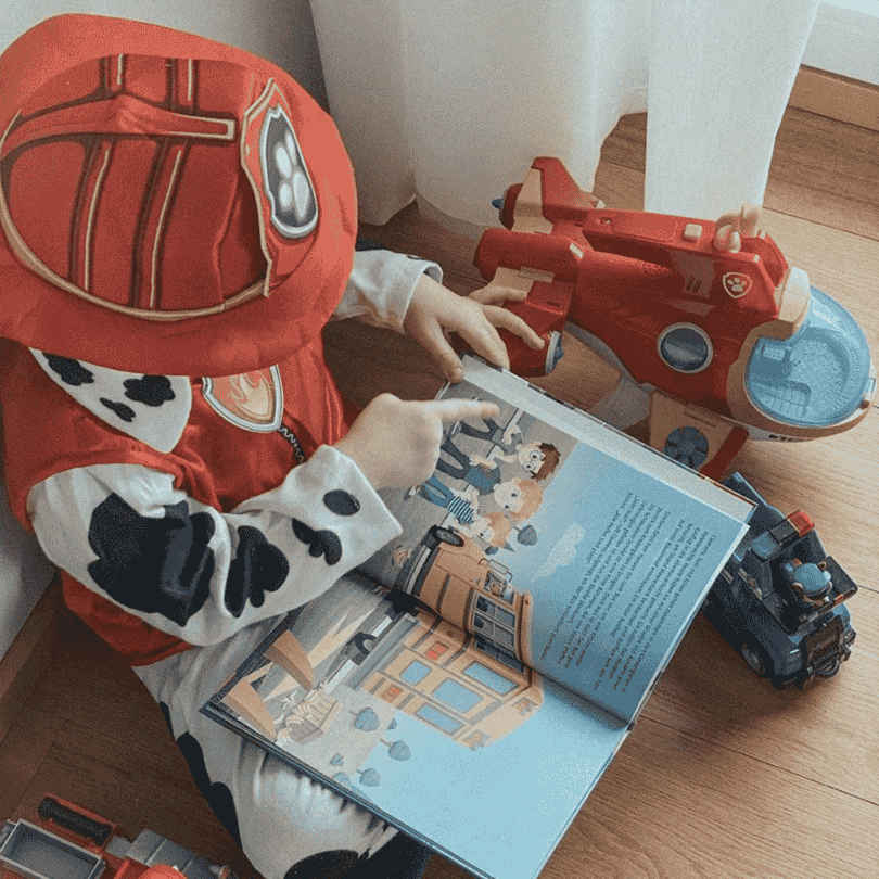 Ein Kind in einem Kostüm sieht sich ein Paw Patrol Buch an