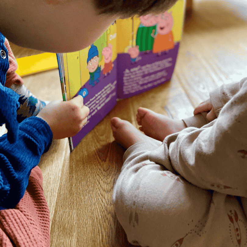 Zwei Kinder sehen sich ein personalisiertes Kinderbuch von Peppa Wutz an