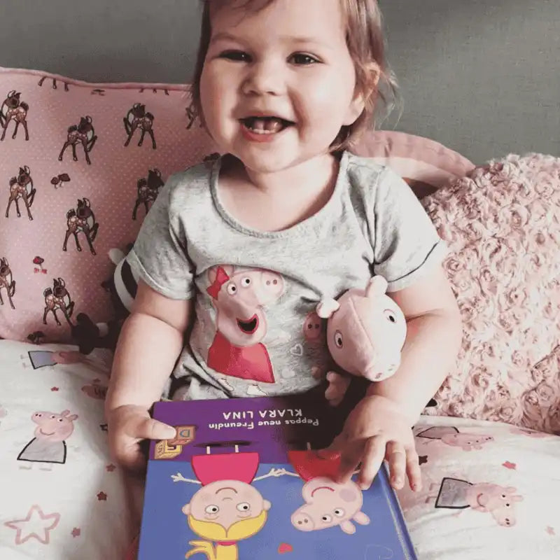 Mädchen mit Peppa-Buch in der Hand and Peppa-Kuscheltier