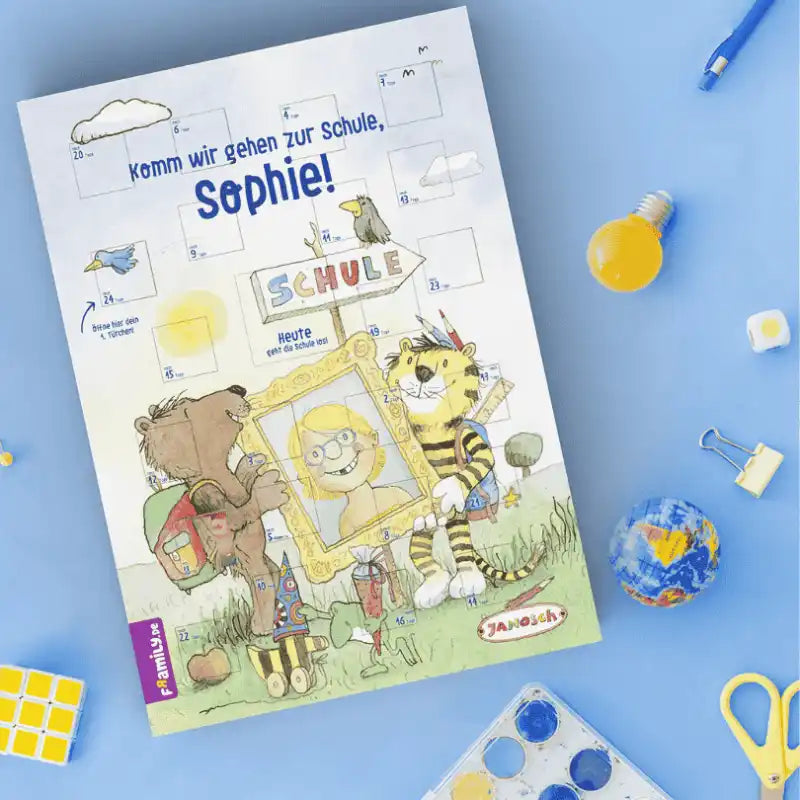 Der Framily Janosch Countdown-Schulstart-Kalender auf blauem Hintergrund, drumherum verteilt sind Schere, Stift, Würfel, Malkasten.