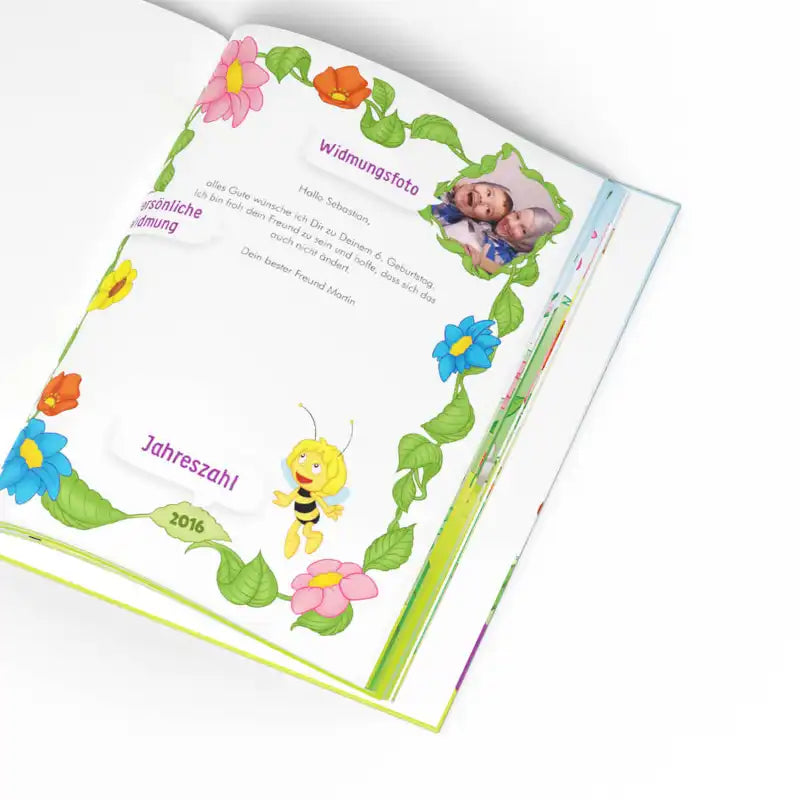 Das offene Kinderbuch "Biene Maja und du" von Framily zeigt bunte Blumen, Biene Maja auf einer Klatschmohnwiese, ein kleines Foto von zwei Kindern in der Ecke, personalisierte Texte und das Jahr 2016 am unteren Rand.