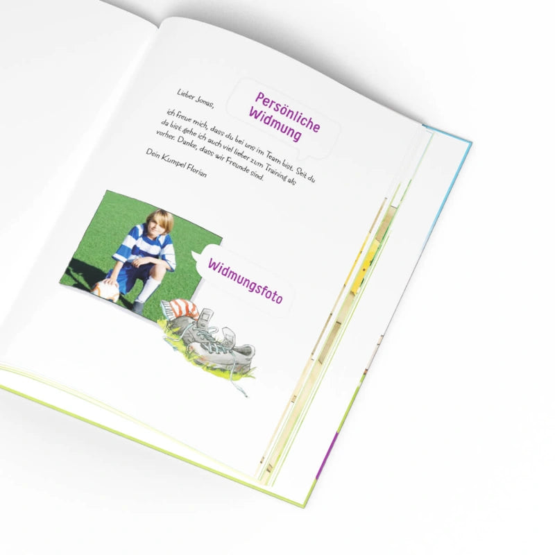 Ein aufgeschlagenes Buch von Framily zeigt eine Seite aus "Deine erste Fußballgeschichte" mit deutschem Text, eine Persönliche Widmung, ein Kinderfoto auf Rasen und eine Illustration von Fußballschuhen und Ball - ideal, um Fußballerinnerungen festzuhalten.