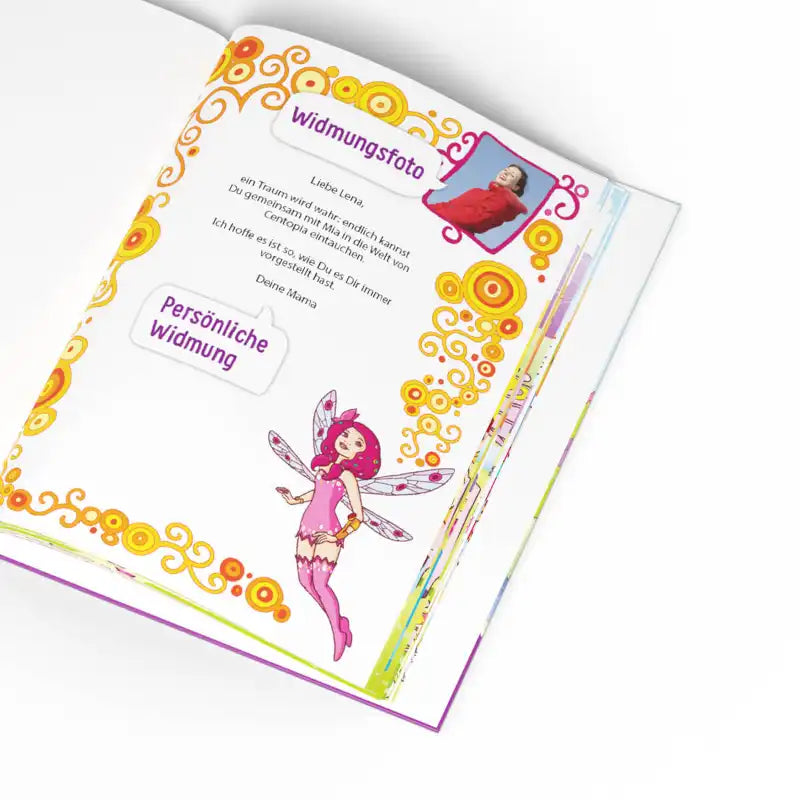 Ein Framily "Mia and me und du"-Kinderbuch zeigt eine bunte Centopia-Fee, einen orange-gelben Rand, ein Kinderfoto und deutsche Textfelder mit der Aufschrift "Widmungsfoto" und "Persönliche Widmung" auf einer weißen Seite.