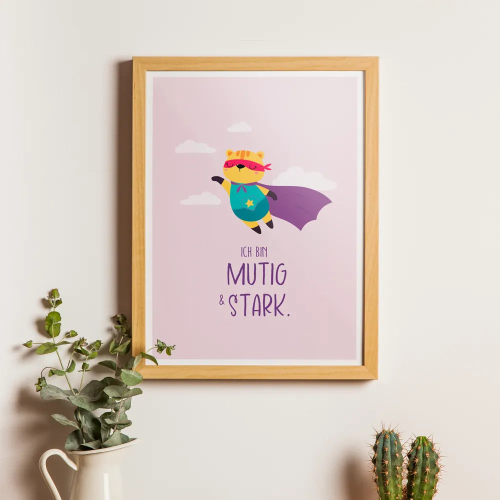 Affirmationsposter Mut hängt mit Bilderrahmen an einer Wand. Auf dem Poster fliegt ein Bär als Superheld durch Wolken über der Affirmation "Ich bin mutig & stark".