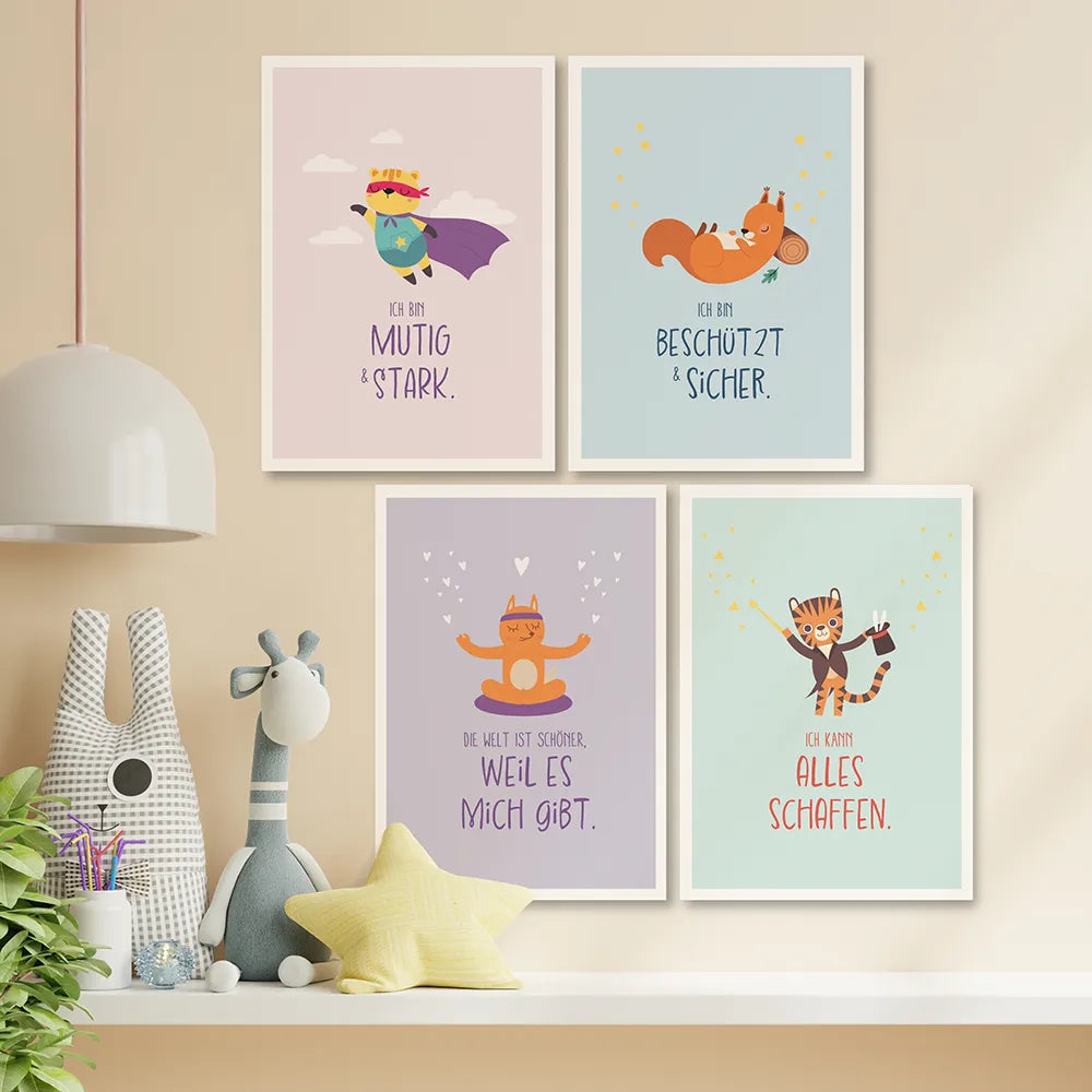 Die Affirmationsposter Mut, Geborgenheit, Selbstliebe und Selbstvertrauen hängen an einer Wand. Daneben eine Lampe und und Kuscheltiere und eine Pflanze.
