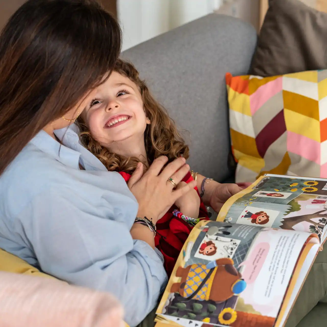 Ein Mädchen schaut freudig zu seiner Mama. Beide lesen das personalisierte Buch von Framily "Ein Brief für dich"