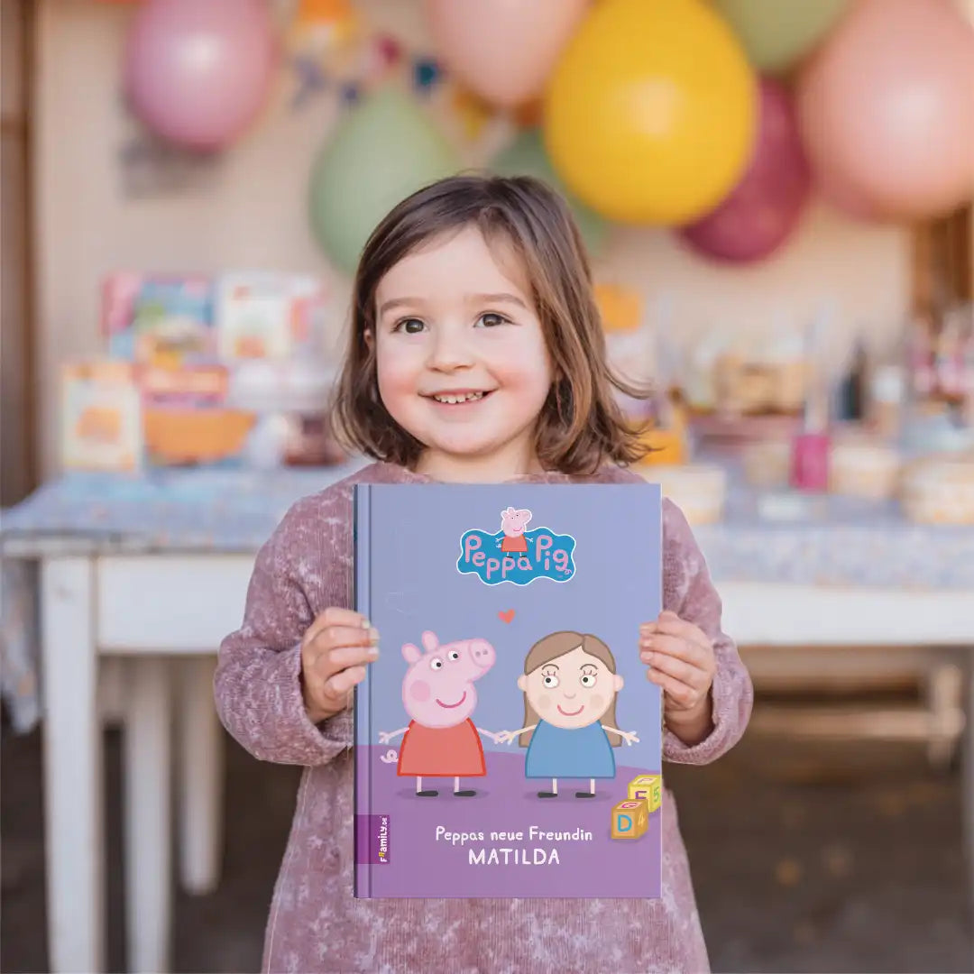 Braunhaariges Mädchen hält freudig strahlend das personalisierte Buch "Peppas neue Freundin Matilda" in den Händen. Im Hintergrund ist ein geschmückter Geburtstagstisch zu sehen.