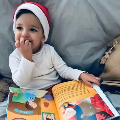 Ein kleiner Junge mit Weihnachtsmütze hält das Buch Dein Weihnachtsmärchen in der Hand und lächelt verschmitzt.